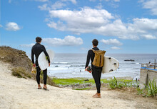 Two Male Surfers Carrying Surfboards Heading To The Beach In Ericeira, Portugal.