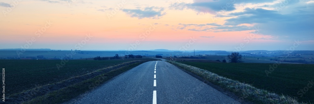 An empty asphalt road (highway) through the fields at sunset. Dramatic sky. France, Europe. Transportation, logistics, travel destinations, tourism, freedom, wanderlust, the way forward concepts - obrazy, fototapety, plakaty 