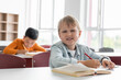 © LIGHTFIELD STUDIOS - happy schoolkid smiling at camera near asian boy writing on blurred background