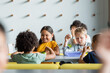 © LIGHTFIELD STUDIOS - cheerful asian girl having breakfast with multiethnic friends in school canteen