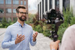 Handsome journalist or news reporter broadcasting on the street. Tv news, reportage concept. Portrait of confident smiling influencer live streaming outdoors