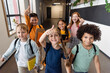 © LIGHTFIELD STUDIOS - cheerful multicultural schoolchildren showing thumbs up in school corridor