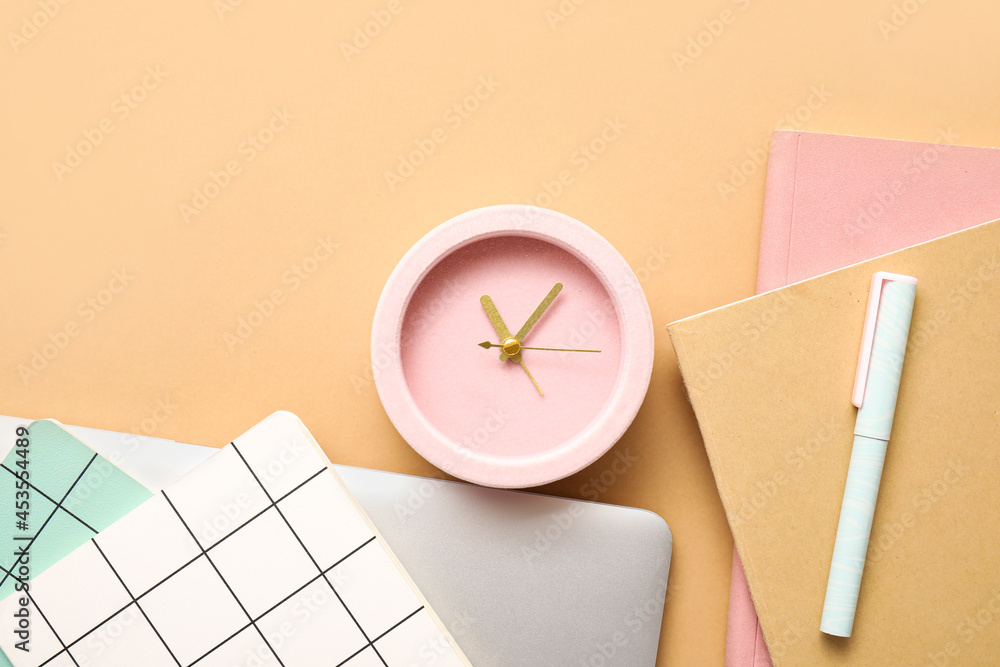 Alarm clock with office supplies and laptop on color background