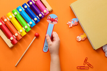 Wall Mural - Hand of child with cute bookmarks and xylophone on color background