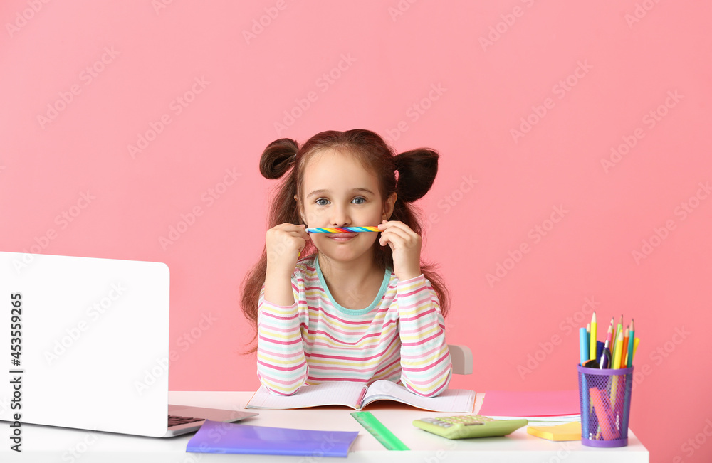Little girl doing homework at table on color background
