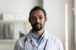 © fizkes - Head shot portrait of confident serious young african american mixed race gp doctor therapist physician in medical coat looking at camera, posing in hospital, medical insurance healthcare concept.