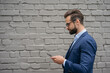 © Oleksii - Young handsome businessman wearing suit and stylish eyeglasses holding mobile phone, communication online isolated on grey background. Bearded man using mobile app, shopping online walking outdoors