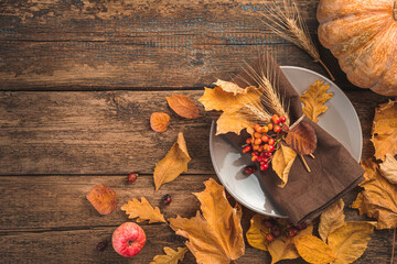 Festive, autumn, culinary background with a plate, cutlery, pumpkin and autumn leaves on a wooden background. Top view, copy space.