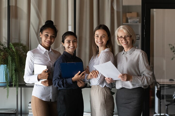 Wall Mural - Portrait of successful diverse businesswomen colleagues group standing in modern office, holding documents, smiling employees business startup team looking at camera, posing for corporate photo