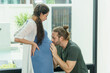 © iammotos - pregnant woman standing with husband kissing to pregnant wife tummy  relax together in living room at home. Take care concept