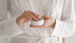 © fizkes - Close up young woman in bathrobe holding moisturizing cream or coconut oil in hands, enjoying body care or facial skincare domestic spa procedures applying lotion vitamin nourishing serum balm.