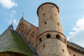 A beautiful old fortress church made of red brick against a blue sky background. A defensive tower with loopholes of a medieval castle.