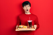 Handsome Hipster Young Man Eating A Tasty Classic Burger With Fries And Soda Afraid And Shocked With Surprise And Amazed Expression, Fear And Excited Face.