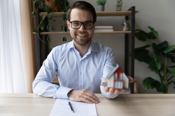 Canvas Print - Happy male real estate or insurance agent holding house miniature, offering property for buying, apartment for rent, giving consultation, helping with mortgage. Head shot portrait