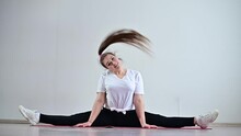 A Young Flexible Fat Woman Sits In A Transverse Twine And Waves Her Hair Against A White Background. Slow Motion