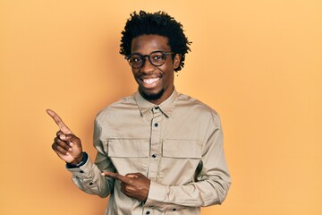 Poster - Young african american man wearing casual clothes and glasses smiling and looking at the camera pointing with two hands and fingers to the side.