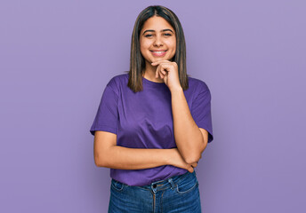 Sticker - Young hispanic girl wearing casual purple t shirt looking confident at the camera with smile with crossed arms and hand raised on chin. thinking positive.