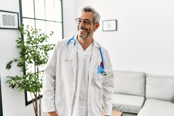 Wall Mural - Middle age hispanic man wearing doctor uniform and stethoscope at waiting room looking away to side with smile on face, natural expression. laughing confident.