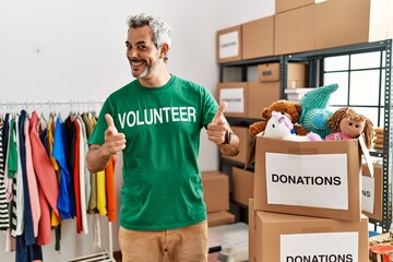 Sticker - Middle age hispanic man wearing volunteer t shirt at donations stand pointing fingers to camera with happy and funny face. good energy and vibes.