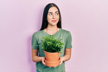 Wall Mural - Beautiful woman with blue eyes holding green plant pot smiling looking to the side and staring away thinking.