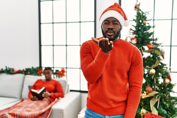 Sticker - Young african american man standing by christmas tree looking at the camera blowing a kiss with hand on air being lovely and sexy. love expression.