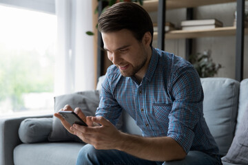 Wall Mural - happy mobile phone user reading text message with good news, smiling at smartphone screen. millennia