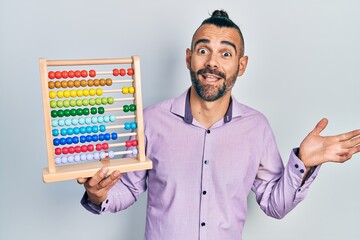 Young hispanic man holding traditional abacus celebrating achievement with happy smile and winner expression with raised hand