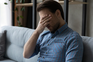 Tired bored millennial guy feeling exhausted, suffering from lack of sleep, laziness, low energy level, hangover. Man touching head, eye, feeling headache. Frustration, exhaustion, fatigue concept