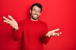 © Krakenimages.com - Handsome man with beard wearing casual red sweater smiling cheerful offering hands giving assistance and acceptance.