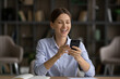 Excited laughing businesswoman looking at phone screen, reading good news, sitting at work desk, overjoyed young woman holding smartphone, received job promotion, reward, online lottery win