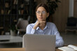 © fizkes - Thoughtful woman in glasses looking to aside, distracted from laptop, sitting at work desk, pensive confident businesswoman or student pondering project strategy, planning workday, visualizing