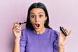 Young hispanic woman holding eyelashes curler afraid and shocked with surprise and amazed expression, fear and excited face.