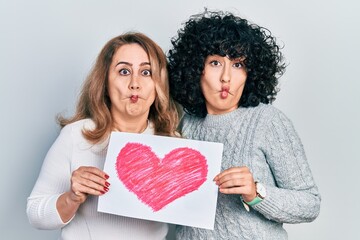 Poster - Middle east mother and daughter holding paper with heart draw making fish face with mouth and squinting eyes, crazy and comical.