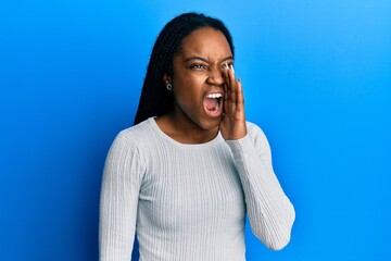 Canvas Print - African american woman with braided hair wearing casual white sweater shouting and screaming loud to side with hand on mouth. communication concept.