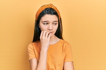 Sticker - Young brunette girl wearing casual orange t shirt looking stressed and nervous with hands on mouth biting nails. anxiety problem.