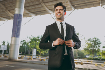 Wall Mural - Bottom view sunlit satisfied confident young traveler businessman man 20s wearing black dinner suit stand outside at international airport terminal look aside. People air flight business trip concept