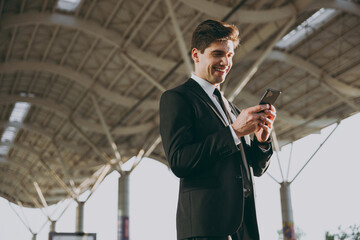 Wall Mural - Bottom view satisfied traveler businessman young man wear black dinner suit stand outside at international airport terminal use mobile phone booking taxi order hotel Air flight business trip concept