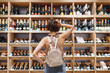 © ViDi Studio - Back view puzzled minded young woman in casual clothes shopping at supermaket grocery store buy choosing wine alcohol bottle scratch head inside hypermarket. People purchasing gastronomy food concept.