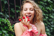 Close Up Young Wistful Happy Satisfied Woman In Pink Dress Put Girl Put Raspberries On Fingers Eat Stand Outdoor Near Forged Gate On Green Ivy Background People Urban Summer Time Lifestyle Concept