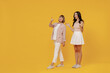 Full body side view two young amazed smiling happy daughter mother together couple women in casual beige clothes walk point index finger aside on workspace isolated on plain yellow background studio