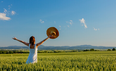 Wall Mural - young girl in hat on a green wheat field and mountains on background