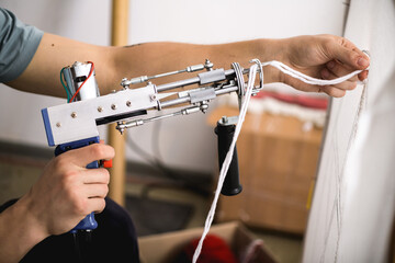 Cropped view of artisan holding thread and rug tufting machine near canvas 