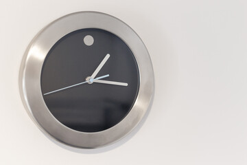 Black wall clock with light blue second hand hanging on the wall. Minimalist flat lay image of metal wall clock side composition.