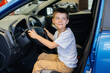 © Andrii - In a car dealership, a happy boy is driving a new car. Car purchase