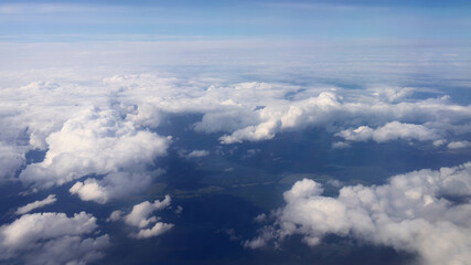 Wall Mural - Flying over fluffy white clouds with a partial view of the rural landscape far beneath. Picturesque cloudscape view from airplane window.