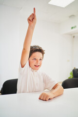 Wall Mural - Little spanish school boy raising hand in class to intervene