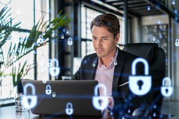Handsome businessman in suit at workplace working with laptop to defend customer cyber security. Concept of clients information protection and brainstorm. Padlock hologram over office background.
