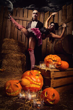 Portrait Of A Man And Sexy Woman Vampires With Halloween Pumpkin Against Wooden Background. Shot In A Studio.