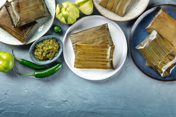 Wall Mural - Tamale, traditional dish of the cuisine of Mexico, various stuffings wrapped in green leaves, top shot with copy space. Hispanic food. With chili peppers and tomatillos