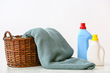 Basket With Knitted Plaid And Detergent On White Background
